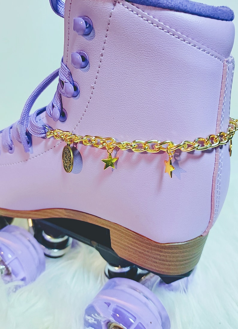 May include: Purple roller skate with a gold chain and star charms around the ankle. The skate has a wooden base and purple wheels.
