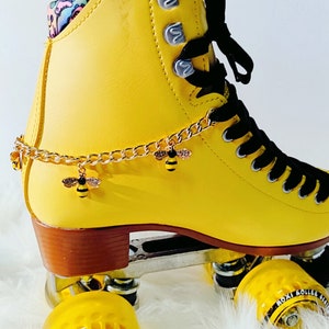 May include: Yellow roller skates with black laces and a gold chain with bee charms. The wheels are yellow with black lettering that says "Moxi Roller Skates".
