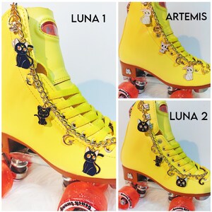 Peut inclure: Patins &agrave; roulettes jaunes avec des breloques de chat noir et blanc sur une cha&icirc;ne dor&eacute;e. Les patins sont &eacute;tiquet&eacute;s "LUNA 1" et "LUNA 2".