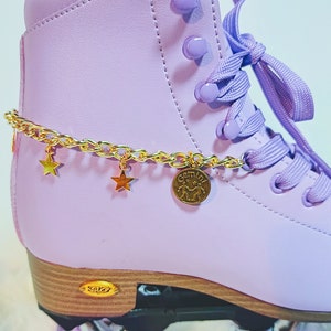 May include: Purple roller skates with gold chain and star charms. The chain has a gold charm with the word "Gemini" and a zodiac symbol.