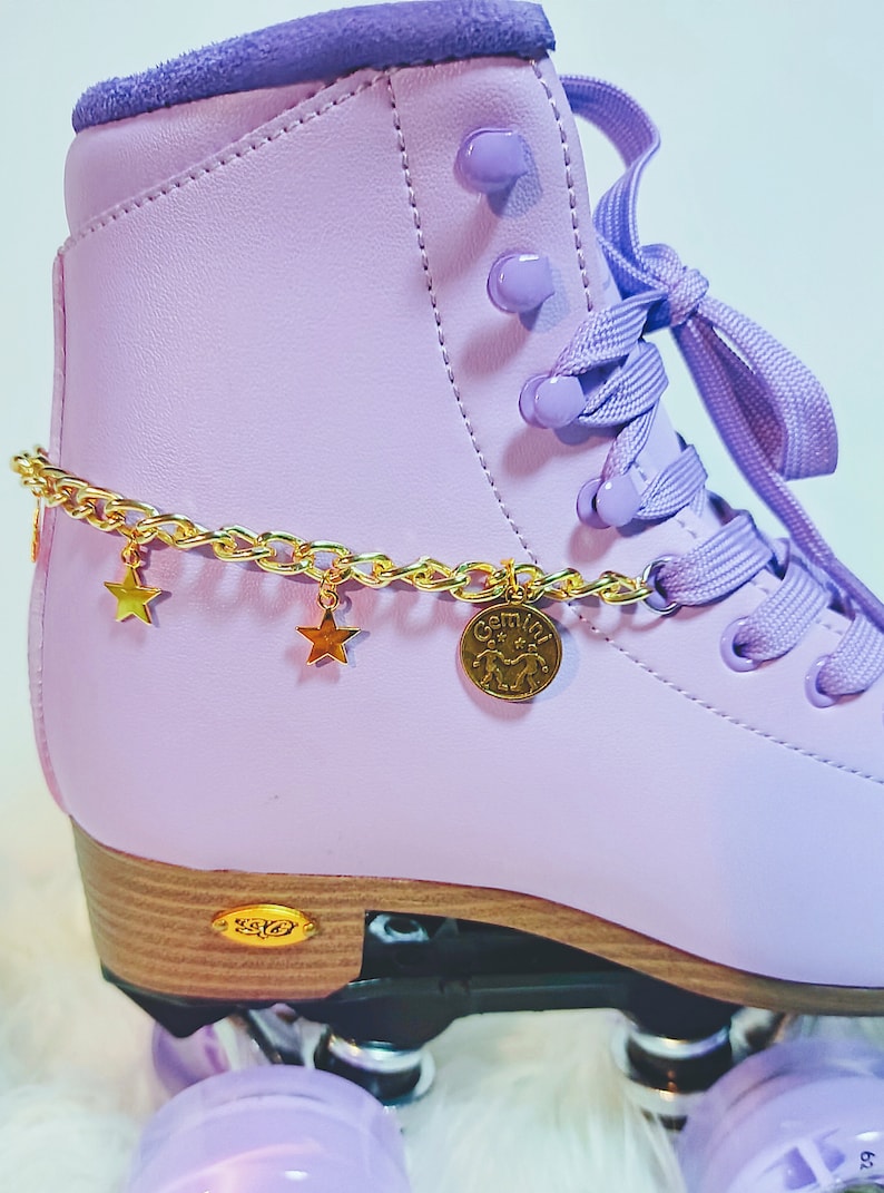 May include: Purple roller skates with gold chain and star charms. The chain has a gold charm with the word "Gemini" and a zodiac symbol.