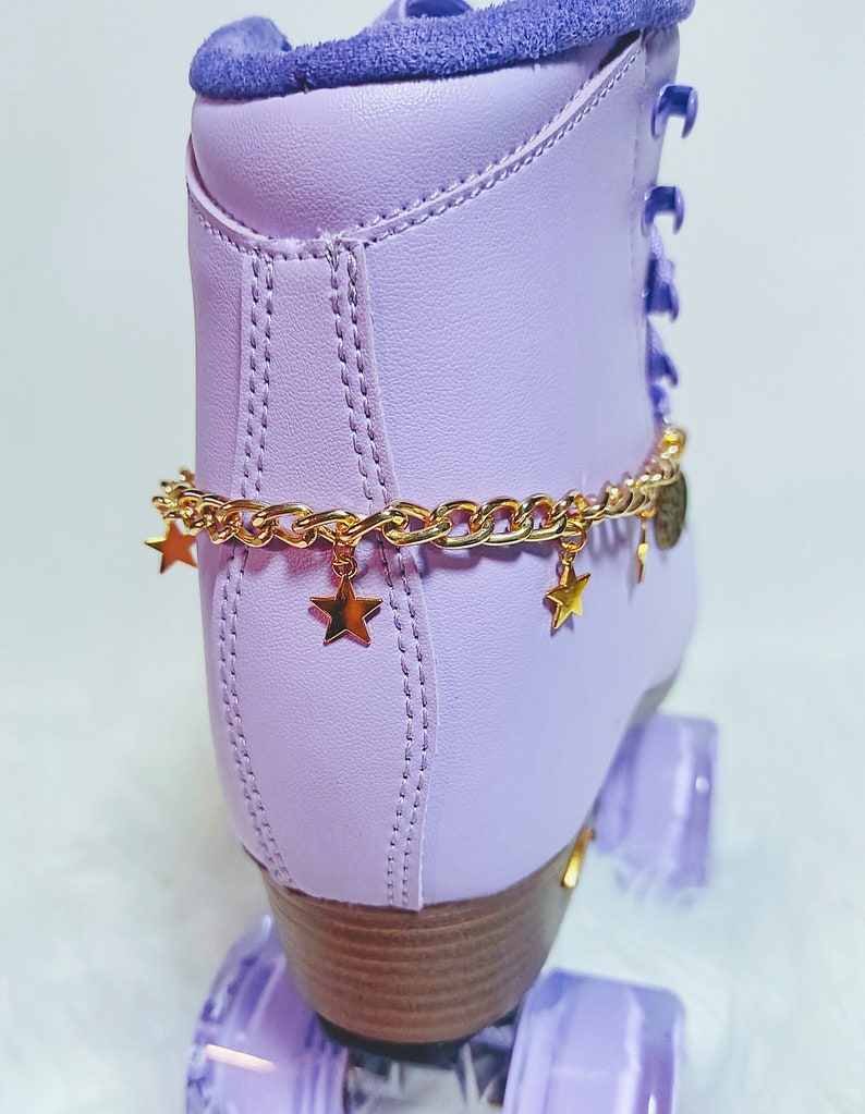 May include: Purple roller skates with gold chain and star charms. The skates have a light purple boot with a brown wooden base and clear purple wheels.