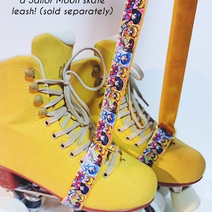 May include: Yellow roller skates with a Sailor Moon skate leash. The leash features a colorful pattern of Sailor Moon characters. The skates have white wheels and beige laces. The text on the image says "Complete the look with a Sailor Moon skate leash!"