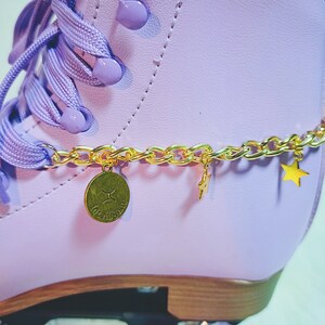 May include: Purple roller skate with a gold chain and charms. The charms include a star and a round charm with the word "twinkle" on it.