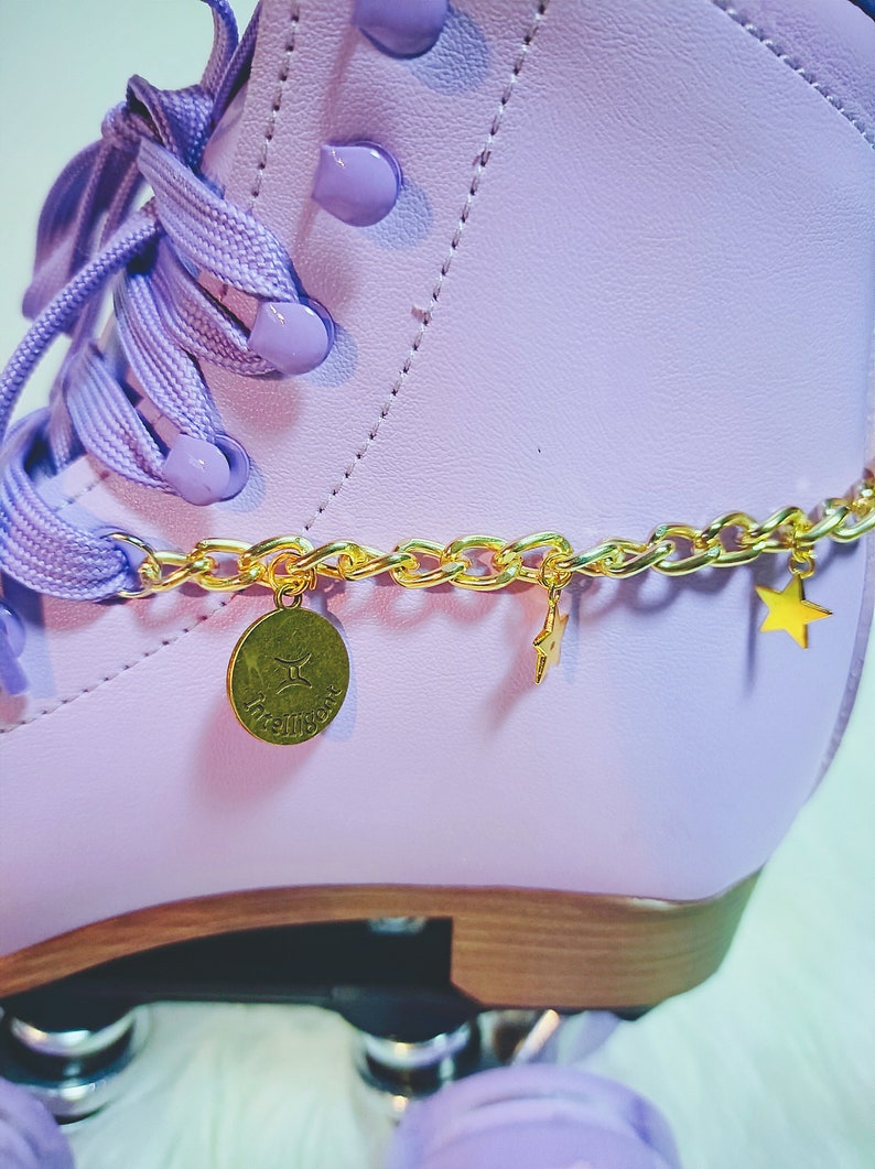 May include: Purple roller skate with a gold chain and charms. The charms include a star and a round charm with the word "twinkle" on it.
