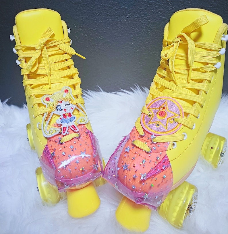 May include: Bright yellow roller skates with matching laces and wheels. Each skate features a decorative patch with a cartoon character and a star design. The toe stops are yellow, and the skates have a star-patterned toe cap.