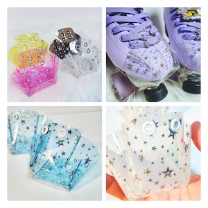 May include: Set of four clear plastic roller skate toe stops with a star pattern and iridescent glitter. The toe stops are in four colours: pink, yellow, blue, and clear.