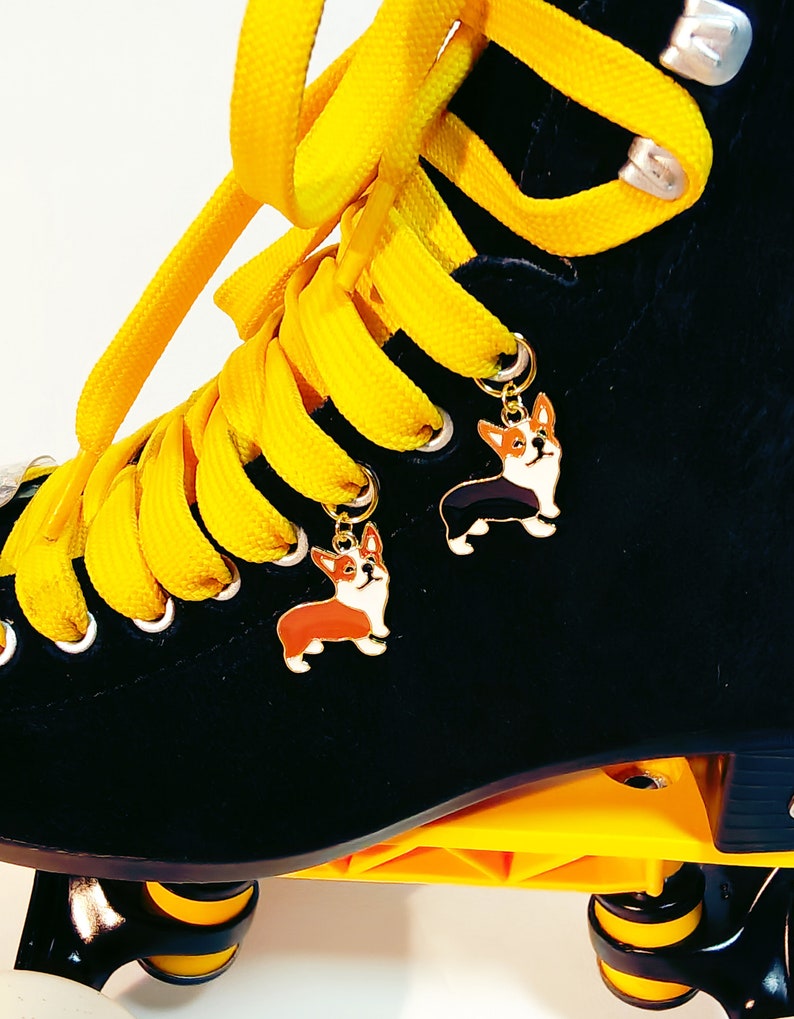 May include: Black roller skates with yellow laces and two small dog charms attached to the laces. The charms are of a black and white corgi and a brown and white corgi.