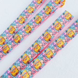 May include: Three pink and blue patterned ribbon straps with a gold metal buckle. The ribbon features a repeating pattern of Spongebob Squarepants characters.