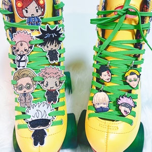 May include: A pair of yellow roller skates with green laces and colourful embroidered anime character charms. The charms are attached to the laces and hang from the skates.