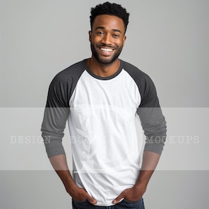 May include: A man wearing a white and grey long-sleeved baseball t-shirt. The shirt has a white front and grey sleeves.