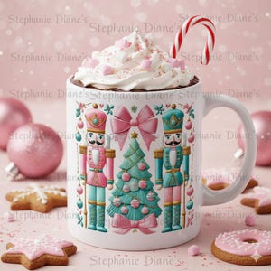 May include: A white ceramic mug filled with hot chocolate, topped with whipped cream, marshmallows, and a candy cane. The mug features a Christmas design with nutcrackers, a Christmas tree, and pink bows. Pink Christmas ornaments and cookies surround the mug.