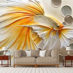 K&ouml;nnte beinhalten: Ein 3D-Wandbild mit einem wei&szlig;en und gelben Fisch mit flie&szlig;enden Flossen vor einem beigefarbenen Hintergrund mit kreisf&ouml;rmigen Formen.
