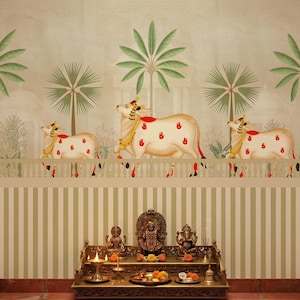 May include: A decorative wall mural featuring three cream-colored cows adorned with red handprints and gold accents. Palm trees and a white fence are also depicted. Below, a golden altar displays religious statues and offerings.