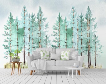 Könnte beinhalten: Ein Aquarellbild eines Waldes in hellblauen und grünen Farbtönen. Das Bild hängt an der Wand hinter einem weißen Sofa mit Kissen und einer Wolldecke. Vor dem Sofa steht ein kleiner Holztisch mit einem Buch und einer Tasse darauf.