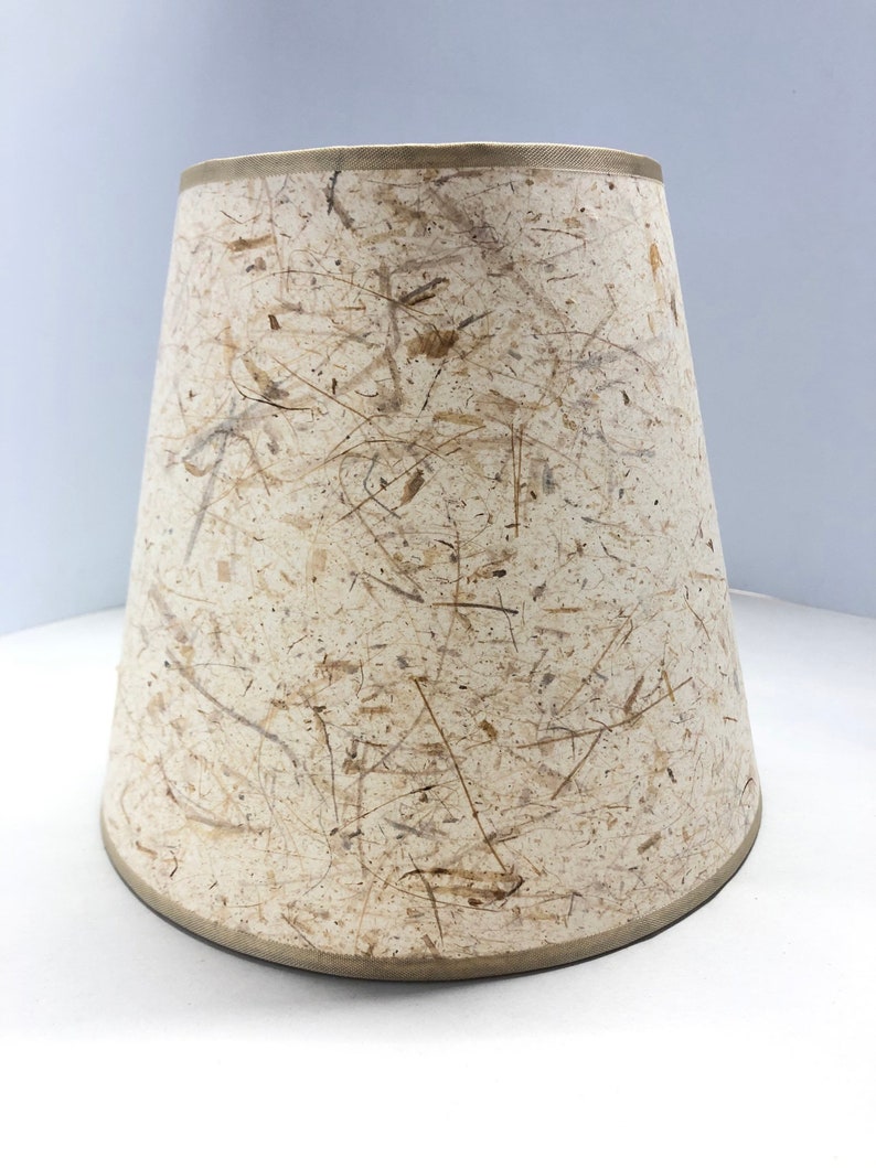 May include: A beige lampshade with a textured surface made of natural fibers. The shade has a slightly curved bottom edge.