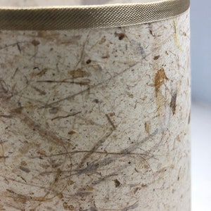 May include: A beige lampshade with a textured surface made of natural fibers. The lampshade has a brown trim around the top edge.