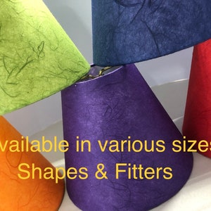 May include: A collection of conical lamp shades in lime green, dark blue, purple, orange, and red, featuring a textured fiber finish and metal hardware. The text "Available in various sizes Shapes & Fitters" is overlaid in yellow on the image.