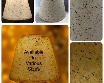 May include: A set of four lampshades made from recycled paper with a speckled pattern. The lampshades are available in various sizes. The lampshades are a light beige color with brown speckles.