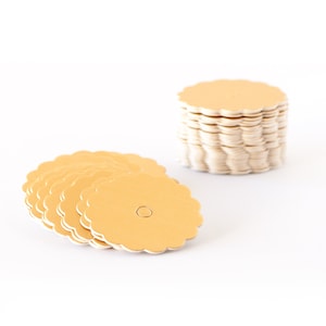 May include: A stack and a spread of scalloped-edge, golden-yellow tags with a small hole in the center. The tags are made of a light-colored paper material and are arranged on a white background.
