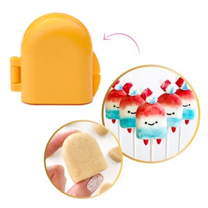 May include: An orange popsicle-shaped cookie cutter next to a group of popsicle-shaped cookies on sticks. The cookies are decorated with red, white, and blue frosting, and have smiling faces.
