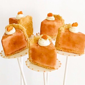 K&ouml;nnte beinhalten: Sechs Mini-K&uuml;rbiskuchen auf wei&szlig;en Kuchenst&auml;ndern. Jeder Kuchen ist mit einem Klecks Schlagsahne und einem kleinen orangefarbenen Bonbon verziert.