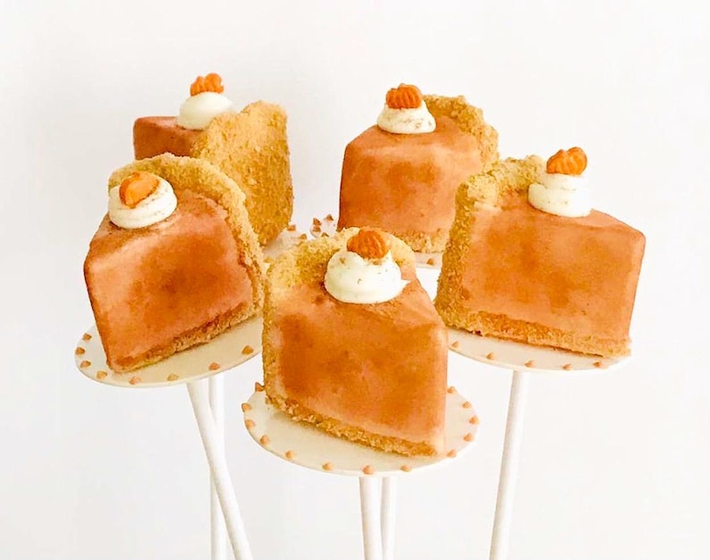 K&ouml;nnte beinhalten: Sechs Mini-K&uuml;rbiskuchen auf wei&szlig;en Kuchenst&auml;ndern. Jeder Kuchen ist mit einem Klecks Schlagsahne und einem kleinen orangefarbenen Bonbon verziert.