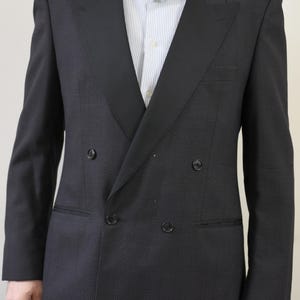 Op de afbeelding: Een donker marineblauwe double-breasted blazer met een zwarte satijnen revers. De blazer heeft een getextureerde weefsel en heeft twee rijen knopen en een borstzak. Een lichtblauw en wit gestreept overhemd is eronder zichtbaar.