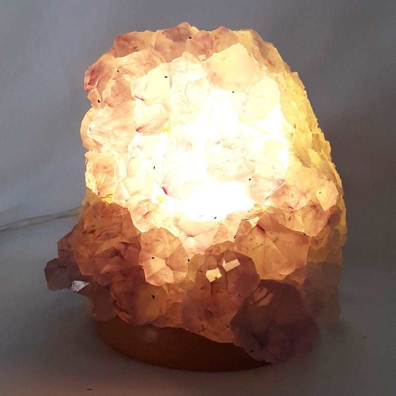 May include: A large, natural amethyst crystal lamp with a wooden base. The crystal is illuminated from within, casting a warm, purple glow.