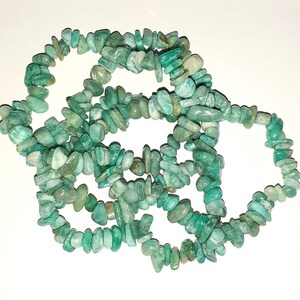 May include: A strand of green aventurine chip beads. The beads are irregular in shape and size, and they are strung together on a clear thread.