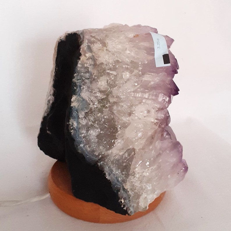 May include: A large amethyst geode with a natural black base, mounted on a wooden base. The geode has a purple and white crystal formation.