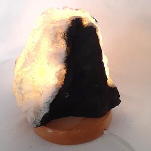 May include: A white and black salt lamp with a wooden base. The lamp is lit and glowing.