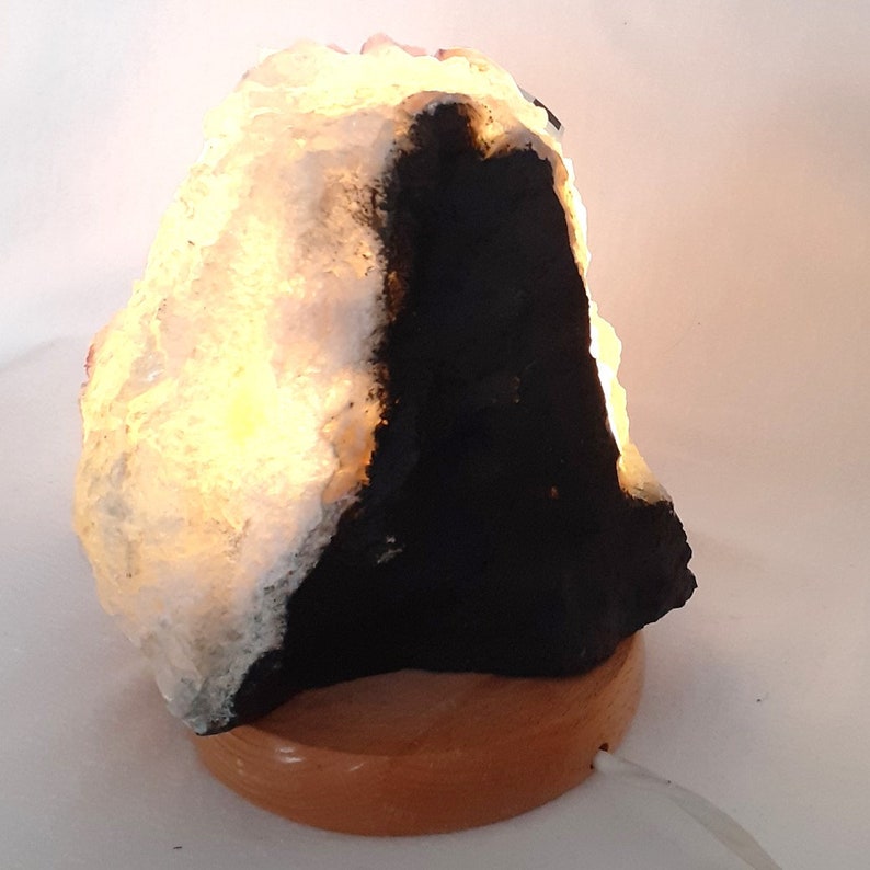 May include: A white and black salt lamp with a wooden base. The lamp is lit and glowing.