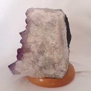 May include: A large amethyst crystal lamp with a wooden base. The crystal is clear with purple accents and has a natural, rough texture.