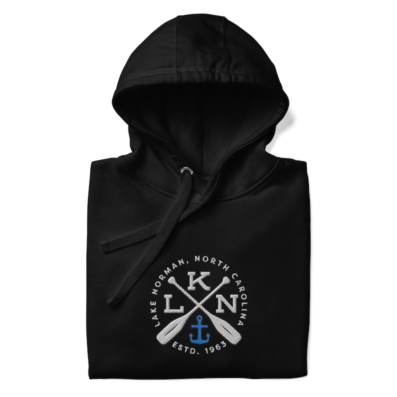 Puede incluir: Sudadera con capucha negra con un logotipo bordado en blanco. El logotipo es un c&iacute;rculo con el texto "Lake Norman, North Carolina" y un dise&ntilde;o de palas cruzadas con un ancla en el centro. El texto "ESTD. 1963" est&aacute; debajo del ancla.