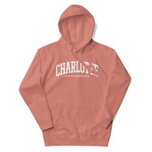 May include: A coral pink hoodie with a white arch design that says "CHARLOTTE NORTH CAROLINA".