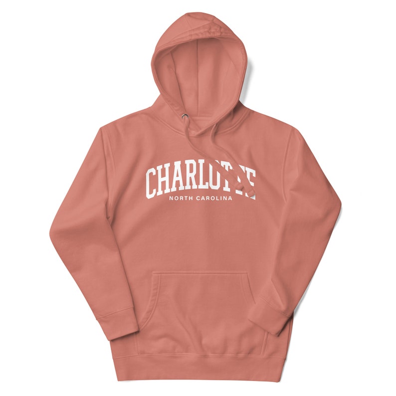 May include: A coral pink hoodie with a white arch design that says "CHARLOTTE NORTH CAROLINA".