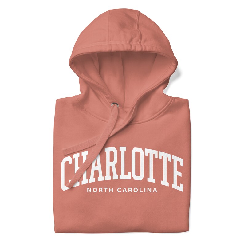 May include: A coral pink hoodie with a white print that says "CHARLOTTE NORTH CAROLINA" in a collegiate font.
