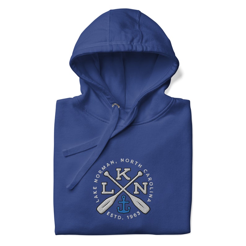 Puede incluir: Sudadera con capucha azul real con un logotipo circular blanco que presenta el texto "Lake Norman, North Carolina" y un dise&ntilde;o de remos cruzados con un ancla en el centro. El texto "ESTD. 1965" est&aacute; debajo del dise&ntilde;o.