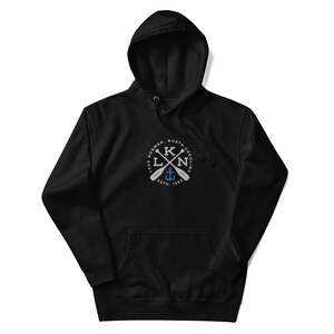 Puede incluir: Sudadera con capucha negra con un gr&aacute;fico blanco de un c&iacute;rculo con el texto "LAKE NORMAN, NORTH CAROLINA" y las letras "KLN" con remos cruzados y un ancla dentro del c&iacute;rculo. El texto "ESTD. 1963" est&aacute; debajo del c&iacute;rculo.