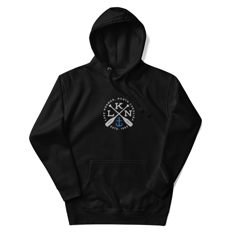 Puede incluir: Sudadera con capucha negra con un gr&aacute;fico blanco de un c&iacute;rculo con el texto "LAKE NORMAN, NORTH CAROLINA" y las letras "KLN" con remos cruzados y un ancla dentro del c&iacute;rculo. El texto "ESTD. 1963" est&aacute; debajo del c&iacute;rculo.