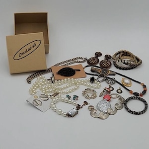 May include: A collection of jewelry including necklaces, bracelets, earrings, and rings. The jewelry features pearls, crystals, and metal accents. A watch and a box with the text "OnceLab 49" are also present.