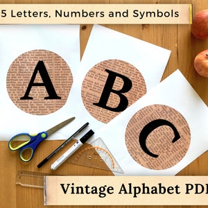 May include: Three white sheets of paper with black circles containing the letters A, B, and C. The circles are made of a vintage newspaper print. The sheets of paper are on a wooden surface with two red apples. The text "45 Letters, Numbers and Symbols" is at the top of the image. The text "Vintage Alphabet PDF" is at the bottom of the image.