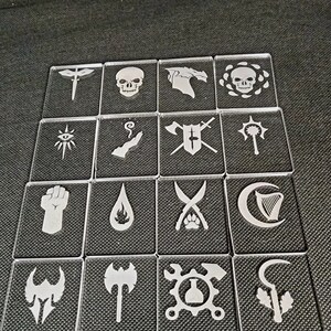 May include: Set of 16 white acrylic tokens with various symbols, including a skull, a sword, a fire, a crescent moon, and a wrench. The tokens are arranged in a grid pattern on a dark gray surface.
