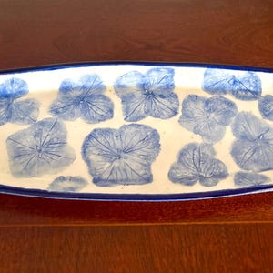 May include: Rectangular ceramic serving tray with a white base and blue floral leaf pattern. The tray has a dark blue border. Ideal for serving or display, it measures approximately 30 cm in length.