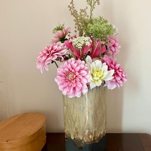 May include: A rectangular vase with a colour gradient, displaying a bouquet of pink and white dahlias and other greenery. The vase transitions from light tan to dark blue at the base. A wooden oval box is visible in the background.