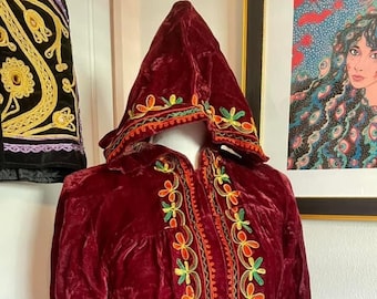 May include: A long, maroon velvet robe with a hood. The robe is embroidered with colourful floral designs in shades of green, yellow, and orange.