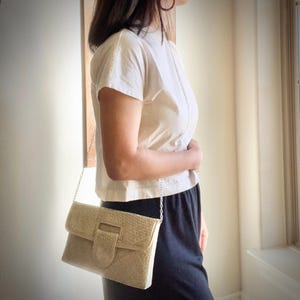 May include: A white woven clutch bag with a silver chain strap. The bag has a flap closure with a silver buckle.