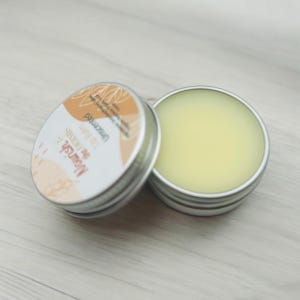 May include: A small silver tin with a yellow lip balm inside. The tin has a label that says "The Monster" and "Lip Butter" in a brown and white font.