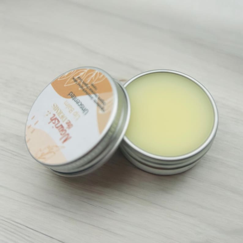 May include: A small silver tin with a yellow lip balm inside. The tin has a label that says "The Monster" and "Lip Butter" in a brown and white font.